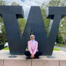 Reham Abuatiq wearing a pink shirt and black pants sitting in front of the University of Washington W logo